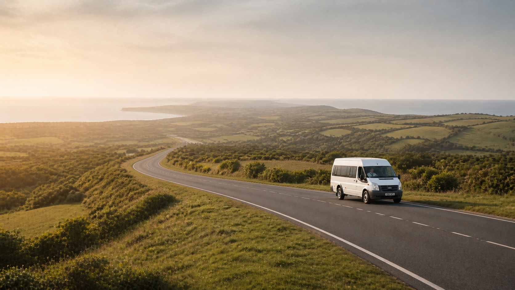 White Ford passenger minibus travelling along a scenic road through the Dorset countryside